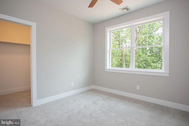 unfurnished bedroom with ceiling fan, light colored carpet, a spacious closet, and multiple windows