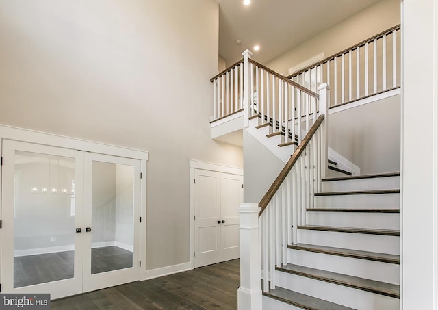 stairs with french doors, a towering ceiling, and wood-type flooring