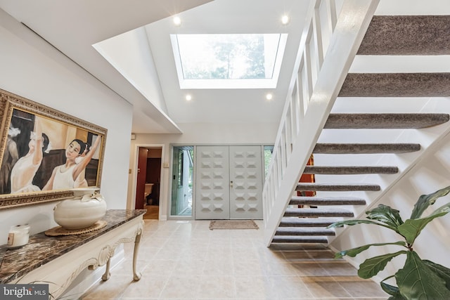 tiled entrance foyer with a skylight, plenty of natural light, high vaulted ceiling, and french doors