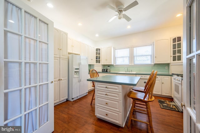 kitchen with white cabinetry, a center island, ceiling fan, white appliances, and a breakfast bar