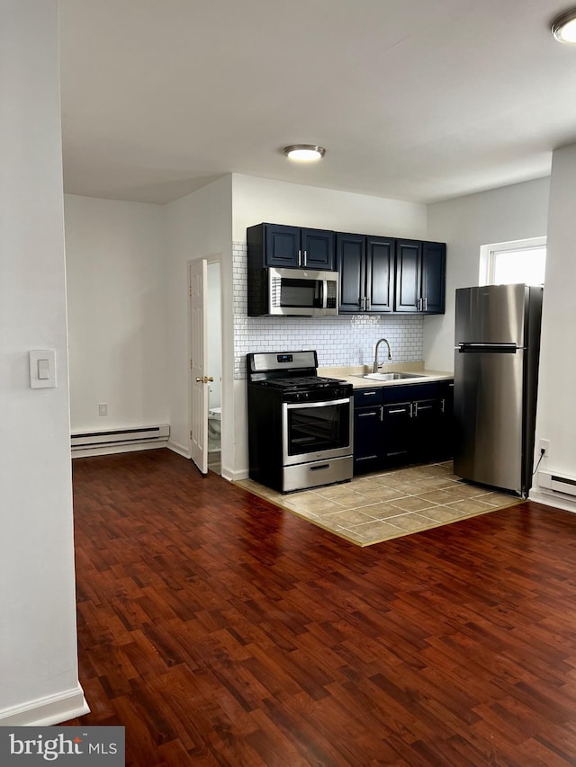 kitchen featuring appliances with stainless steel finishes, a baseboard heating unit, sink, tasteful backsplash, and hardwood / wood-style flooring