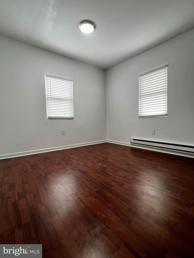 empty room with dark hardwood / wood-style flooring and a baseboard radiator