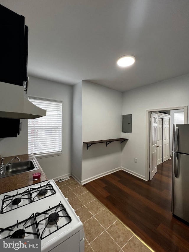 kitchen with stove, tile floors, extractor fan, sink, and stainless steel fridge