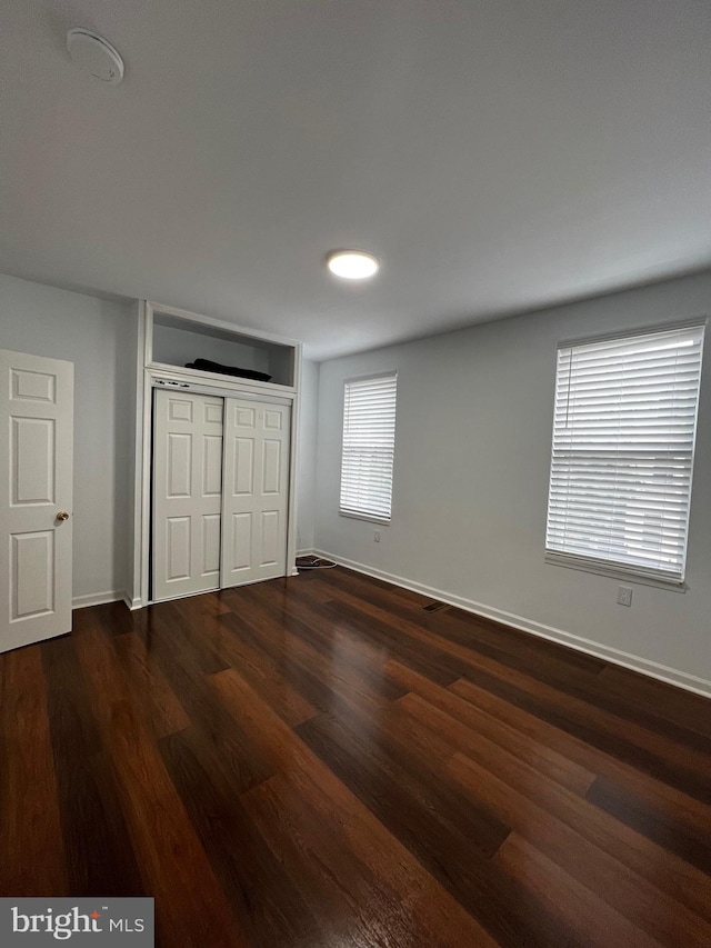 unfurnished bedroom with dark wood-type flooring, a closet, and multiple windows