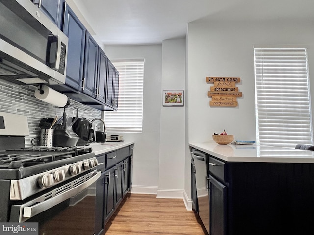 kitchen with appliances with stainless steel finishes, sink, light hardwood / wood-style floors, tasteful backsplash, and blue cabinetry