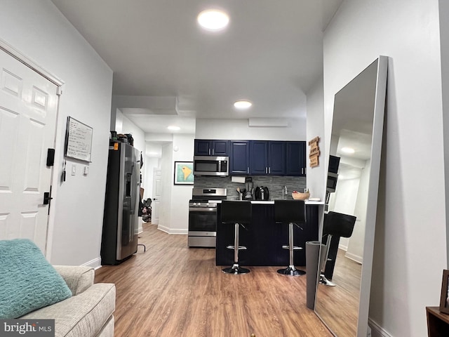 kitchen featuring kitchen peninsula, appliances with stainless steel finishes, backsplash, light hardwood / wood-style floors, and blue cabinets