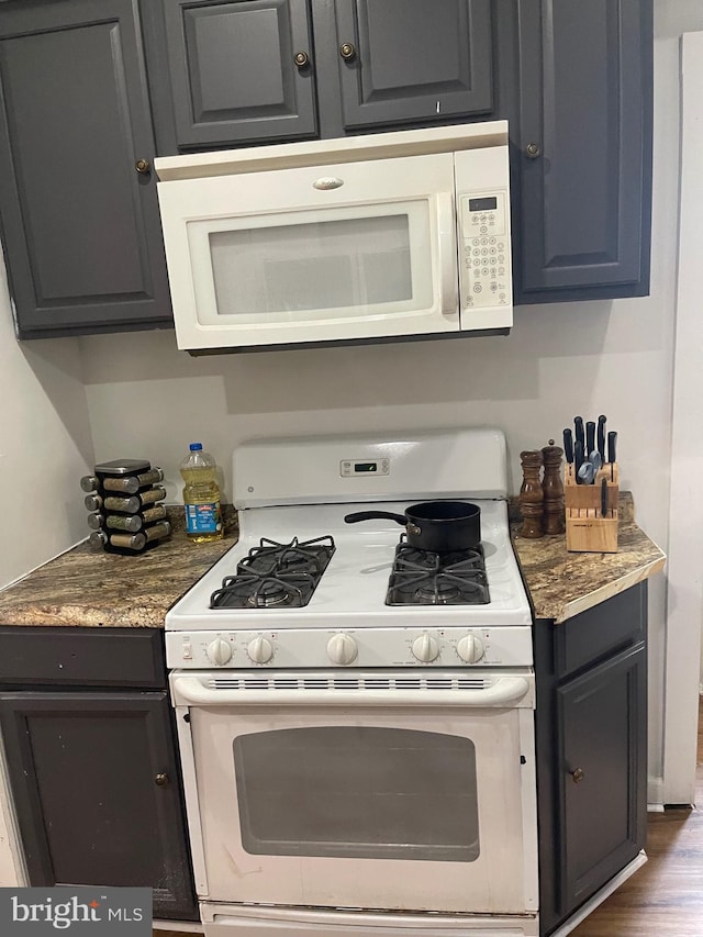 kitchen with stone counters, dark hardwood / wood-style floors, and white appliances