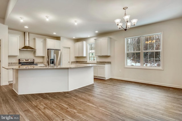 kitchen with white cabinetry, wall chimney range hood, pendant lighting, a kitchen island with sink, and appliances with stainless steel finishes