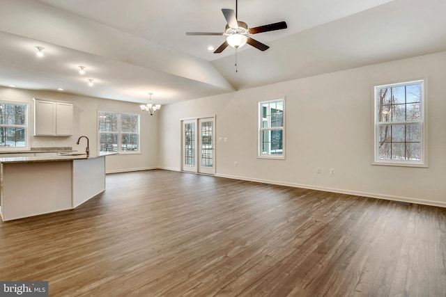 unfurnished living room with sink, dark wood-type flooring, plenty of natural light, vaulted ceiling, and ceiling fan with notable chandelier