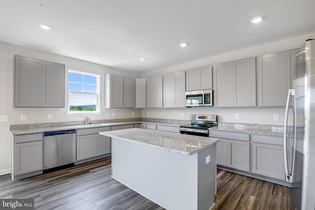 kitchen featuring light stone counters, appliances with stainless steel finishes, a center island, gray cabinets, and dark wood-type flooring