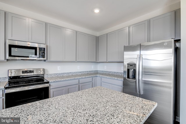 kitchen featuring hardwood / wood-style flooring, appliances with stainless steel finishes, gray cabinets, and light stone counters