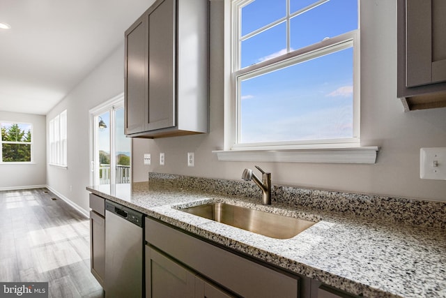 kitchen featuring light hardwood / wood-style flooring, dishwasher, sink, and light stone countertops