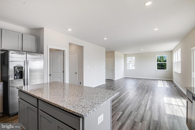 kitchen with a center island, stainless steel refrigerator with ice dispenser, light stone countertops, gray cabinetry, and hardwood / wood-style flooring