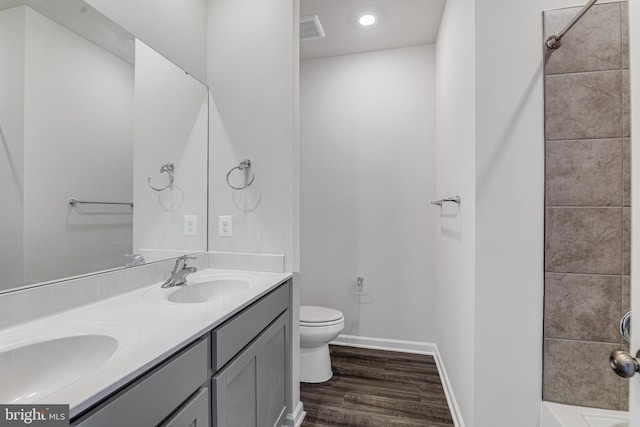 full bathroom with hardwood / wood-style flooring, tiled shower / bath, double vanity, and toilet