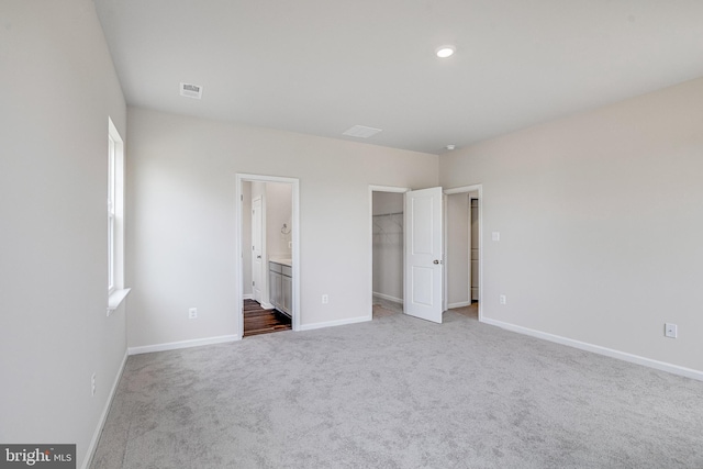 unfurnished bedroom with carpet flooring, a closet, a spacious closet, and ensuite bathroom