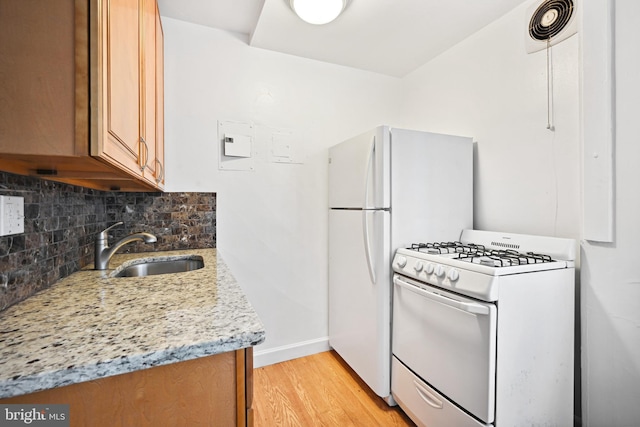 kitchen with light hardwood / wood-style flooring, white appliances, light stone counters, sink, and tasteful backsplash