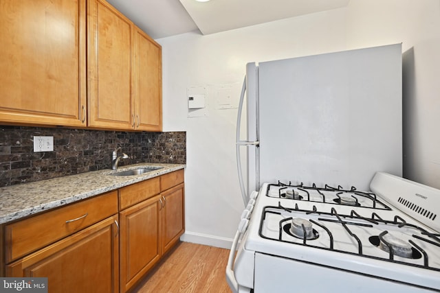 kitchen featuring light stone countertops, light hardwood / wood-style floors, range, backsplash, and sink