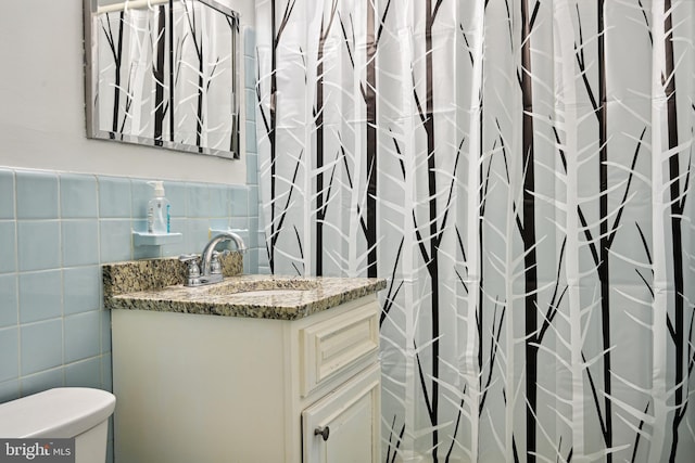 bathroom featuring vanity with extensive cabinet space, toilet, and tile walls