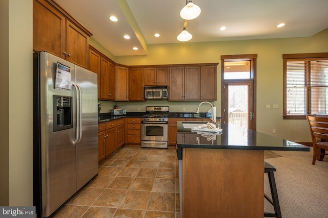 kitchen featuring sink, hanging light fixtures, stainless steel appliances, a kitchen bar, and a center island with sink