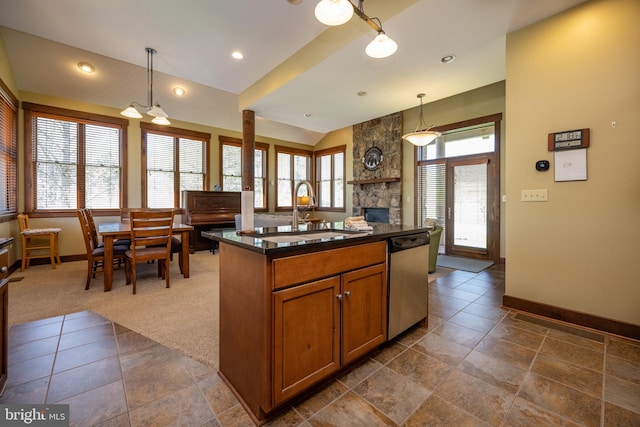 kitchen with stainless steel dishwasher, a kitchen island with sink, sink, a stone fireplace, and hanging light fixtures