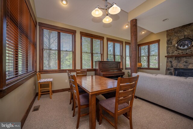 dining room with a stone fireplace, light colored carpet, a wealth of natural light, and vaulted ceiling