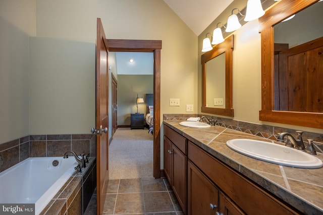 bathroom featuring vanity, tiled tub, and vaulted ceiling