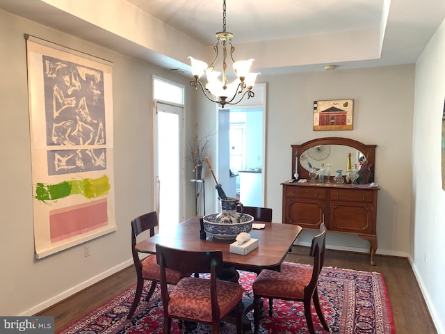 dining room with dark hardwood / wood-style flooring, a raised ceiling, and a chandelier