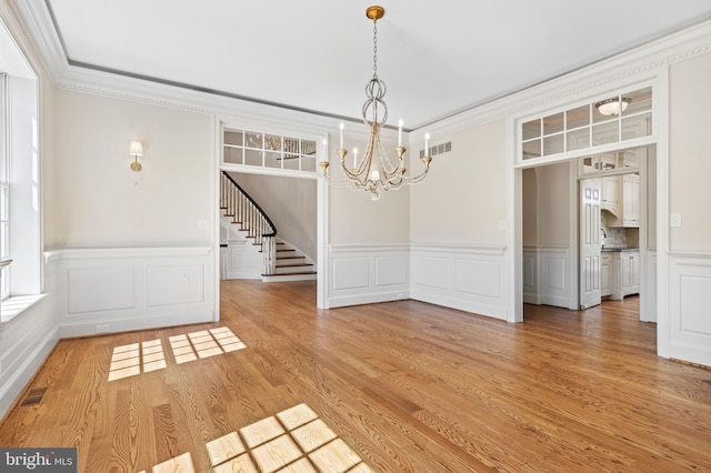 unfurnished dining area featuring wood-type flooring, an inviting chandelier, and ornamental molding