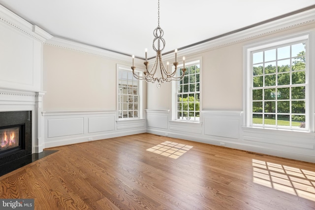 unfurnished dining area with wood-type flooring, crown molding, and a notable chandelier