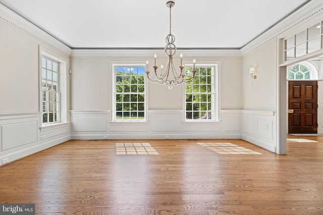 unfurnished dining area featuring a healthy amount of sunlight, light wood-type flooring, ornamental molding, and an inviting chandelier