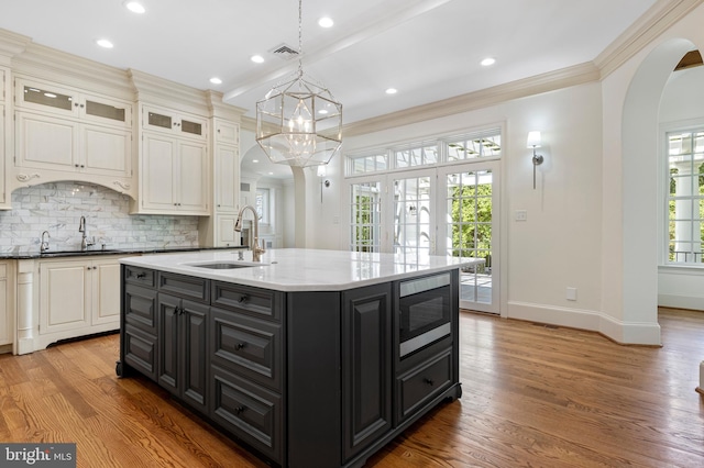 kitchen featuring stainless steel microwave, sink, a kitchen island with sink, and light hardwood / wood-style flooring