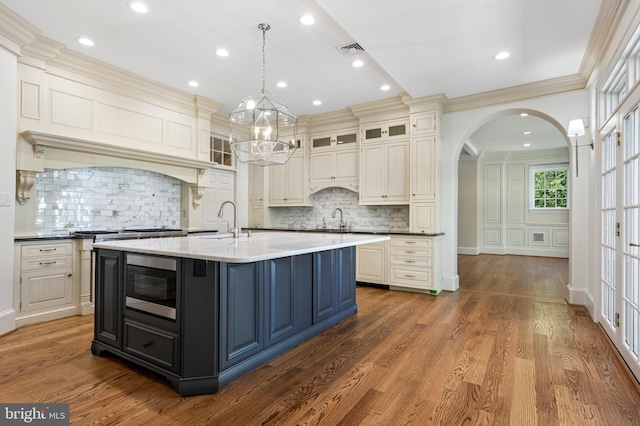 kitchen with ornamental molding, pendant lighting, dark hardwood / wood-style floors, stainless steel microwave, and an island with sink