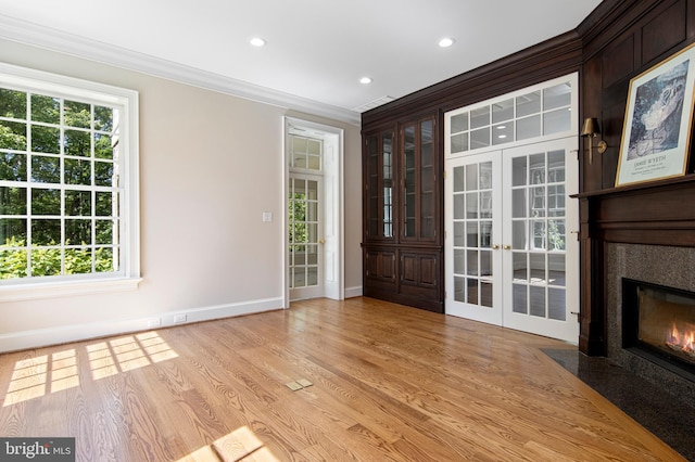 interior space with french doors, a high end fireplace, light hardwood / wood-style floors, and ornamental molding