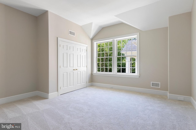 unfurnished bedroom featuring light carpet, a closet, and lofted ceiling