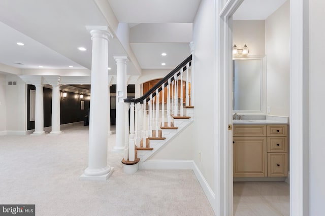 stairway with ornate columns, sink, and carpet