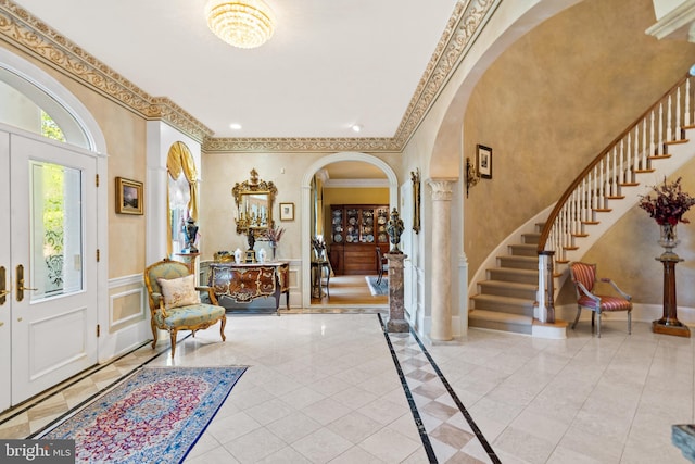 foyer entrance featuring light tile patterned flooring, ornate columns, and crown molding