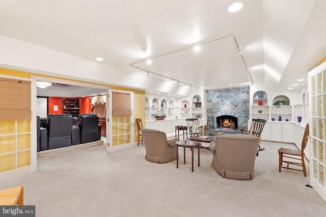 carpeted living room featuring track lighting, built in shelves, a textured ceiling, a stone fireplace, and lofted ceiling