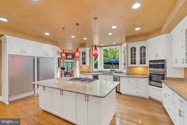 kitchen with white cabinetry, hanging light fixtures, stainless steel appliances, light hardwood / wood-style flooring, and a kitchen island