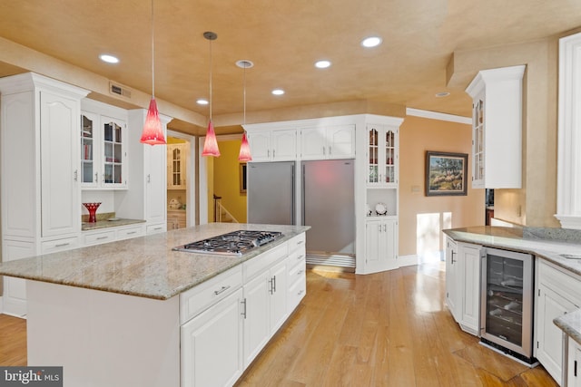 kitchen featuring beverage cooler, a kitchen island, decorative light fixtures, light hardwood / wood-style floors, and stainless steel gas cooktop