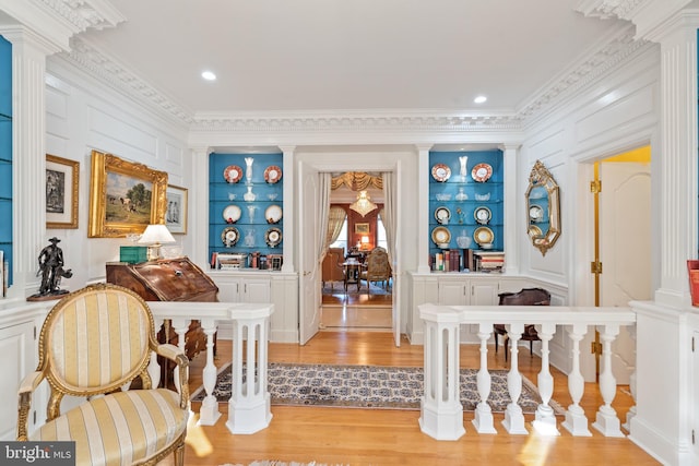 sitting room with built in shelves, light wood-type flooring, decorative columns, and crown molding