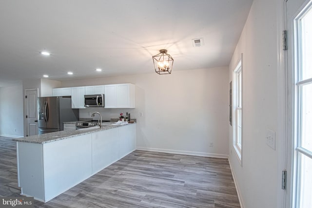 kitchen with kitchen peninsula, white cabinetry, light wood-type flooring, and stainless steel appliances