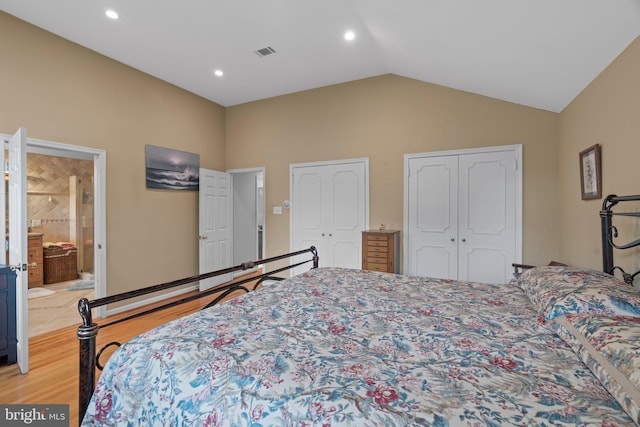 bedroom featuring lofted ceiling, two closets, ensuite bathroom, and light wood-type flooring