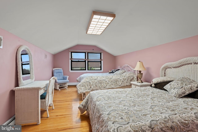 bedroom with a baseboard heating unit, light hardwood / wood-style flooring, and vaulted ceiling