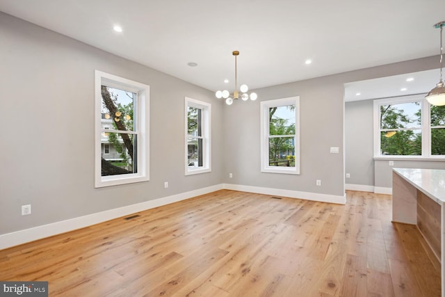 unfurnished dining area featuring a notable chandelier, light hardwood / wood-style floors, and a wealth of natural light