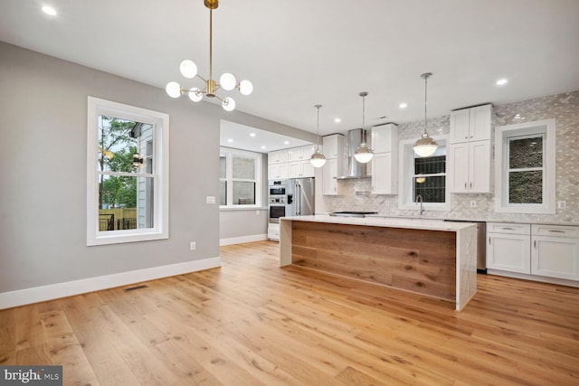 kitchen with light hardwood / wood-style floors, white cabinetry, wall chimney range hood, a kitchen island, and pendant lighting