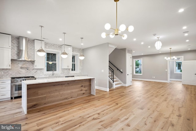 kitchen featuring hanging light fixtures, light wood-type flooring, white cabinets, wall chimney exhaust hood, and high end stainless steel range oven