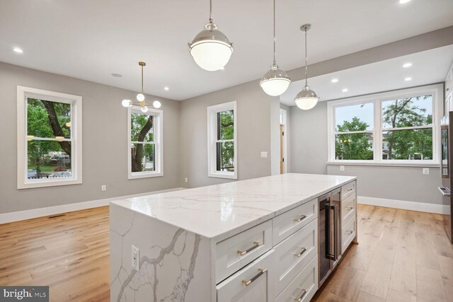 kitchen featuring a center island, beverage cooler, decorative light fixtures, and light wood-type flooring