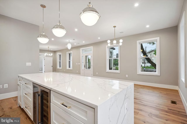 kitchen with a center island, decorative light fixtures, light stone counters, and light hardwood / wood-style flooring