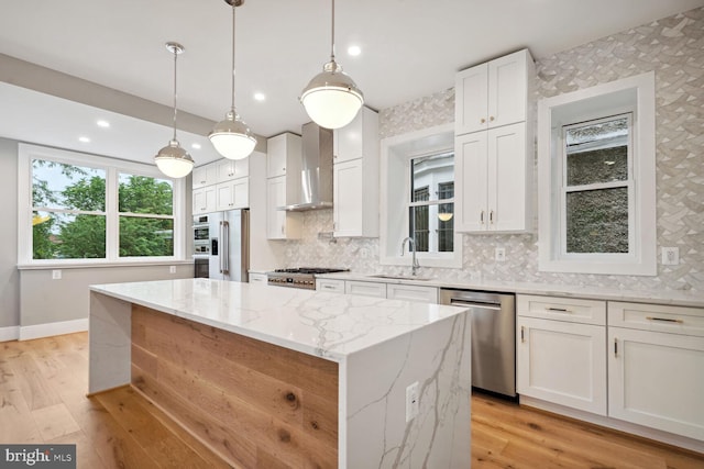 kitchen featuring a center island, hanging light fixtures, stainless steel appliances, light hardwood / wood-style flooring, and wall chimney exhaust hood