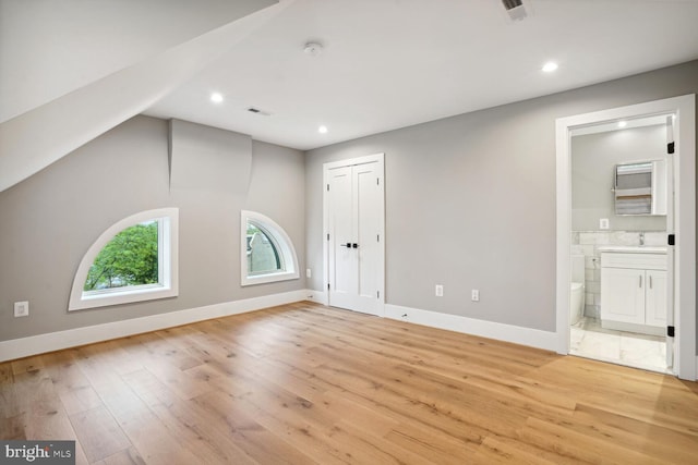 interior space featuring sink, light hardwood / wood-style floors, ensuite bath, and vaulted ceiling